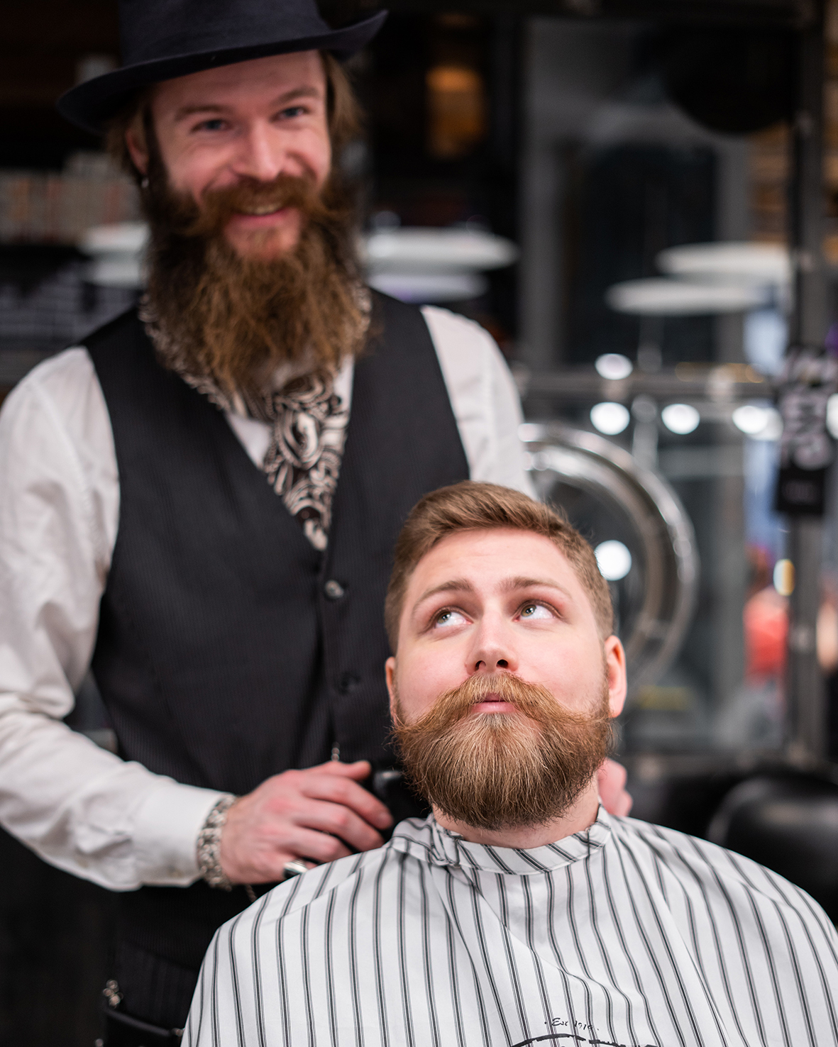 Zákazník u barbera sedí v kresle a bradu má upravenú pomocou balzamu na fúzy. Za ním stojí jeho holič.